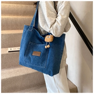 Detail of blue denim tote bag with leather logo tag and toast plush charm accessory