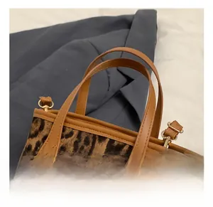 Detail showing the leopard print fabric with brown leather handle and gold metal hardware