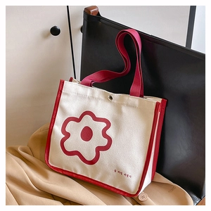 Detail of canvas tote bag with red flower graphic and sturdy handles on leather chair