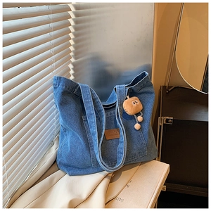 Detailansicht der blauen Denim-Tragetasche mit Lederlogo und braunem Plüschanhänger
