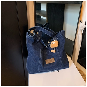 Détail d'un sac cabas en denim bleu foncé avec patch logo en cuir et charme en peluche