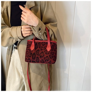 Close-up of leopard print bucket bag with red handles worn with a beige trench coat