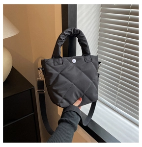 Detail of black quilted nylon handbag with white decorative button and padded handle