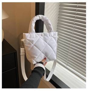Detail of white quilted handbag with padded texture and adjustable fabric shoulder strap