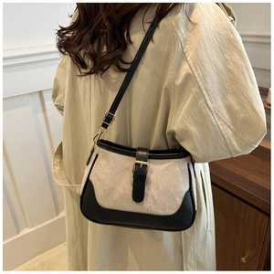 Detail of beige canvas shoulder bag featuring black leather trim and golden buckle