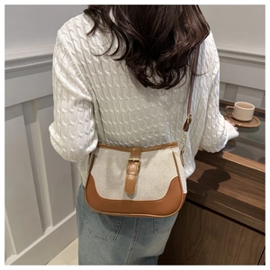 Detail of beige canvas and brown leather saddle bag styled with a white cable knit sweater