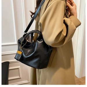 Close-up of black pleated PU leather bucket bag with mini charm on a khaki trench coat