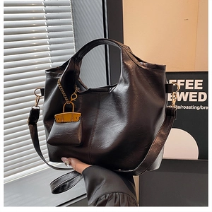 Close-up of black grainy leather texture and golden chain mini bag pendant on a soft bucket bag