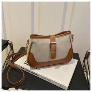 Detail of canvas shoulder bag with brown leather trim and golden metal buckle on a book