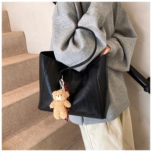 Detail of black faux leather tote bag with vertical stitching and plush bear charm