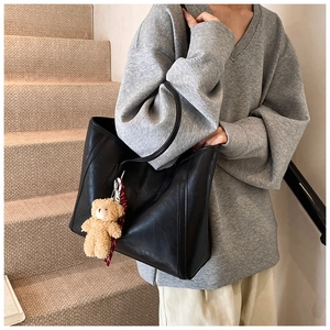 Detail of black leather tote bag with plush bear charm and silk scarf on the side