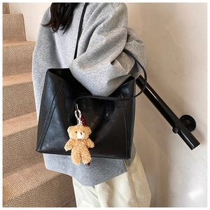 Close-up of black PU leather tote bag with cute brown plush bear charm accessory