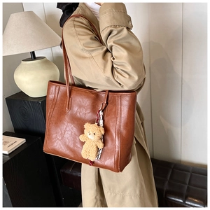 Detail of dark brown leather tote bag with teddy bear charm and plaid scarf on model