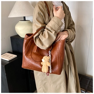 Close-up of vintage brown leather tote bag with cute plush bear pendant accessory