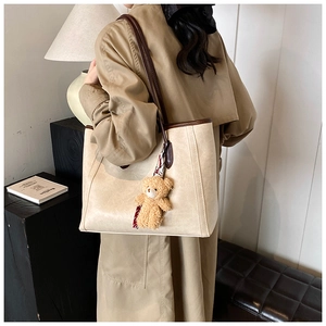 Model wearing a large cream tote bag with dark brown trim and a plush bear pendant charm