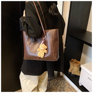 Detail of dark brown faux leather tote bag with cute bear charm worn over the shoulder