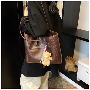 Detail view of deep brown faux leather tote bag with stylish teddy bear keychain charm