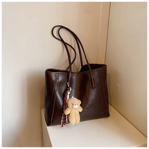 Macro view of vintage brown tote bag featuring a cute teddy bear charm and red plaid ribbon