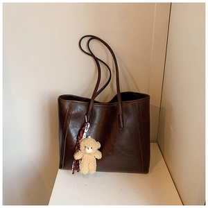 Detail of dark brown tote bag with glossy faux leather texture and plush bear pendant