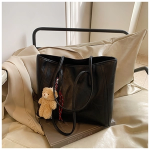 Detail of large black leather tote bag with a cute brown bear charm and plaid ribbon