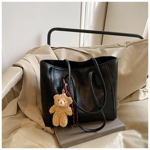 Close-up of black leather tote bag with a plush bear charm on books in home setting