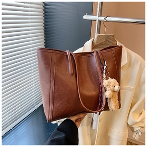 Detailed macro view of brown PU leather tote bag with a cute plush bear charm