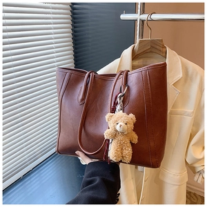 Detail of dark brown leather tote bag featuring a cute beige plush bear pendant charm