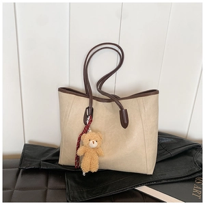Detail of cream tote bag with brown straps and a cute plush bear charm on leather base