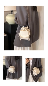 Detail of cream square bucket bag with pearl handle and gold chain strap on model