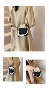 Close-up of a black box bag featuring a pearl handle and gold chain strap detail