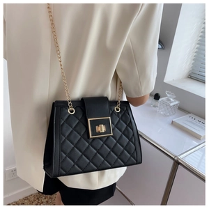 Detail of black quilted crossbody bag with golden chain strap and turn-lock closure
