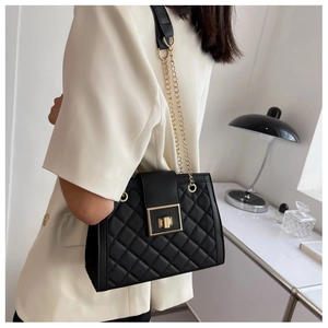 Close-up of black quilted crossbody bag with gold square twist lock and metal chain strap