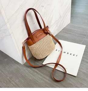 Dettaglio borsa in paglia intrecciata con finiture in pelle marrone e logo dorato