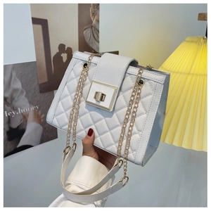 Close-up of white quilted leather texture with square golden twist-lock and chain strap