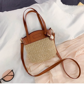 Dettaglio della borsa a secchiello in paglia con patchwork in pelle marrone e logo