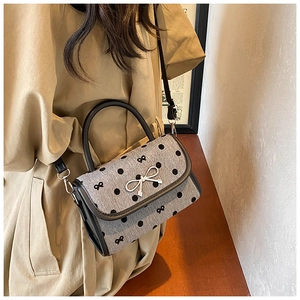 Woman wearing a grey polka dot crossbody bag with a silver bow clasp in a cozy cafe