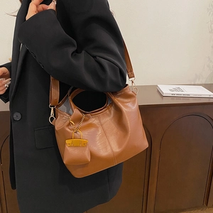 Brown lychee-grain leather bucket bag with a wide shoulder strap and matching mini charm