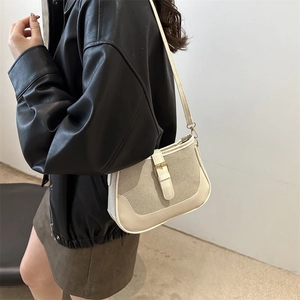Chic beige canvas and leather underarm bag worn by model over a black jacket
