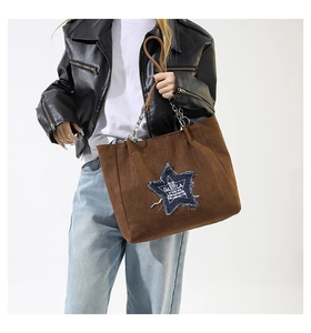 Detail of a dark brown tote bag featuring a star-shaped denim patch and chain strap