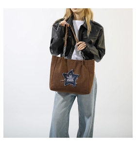 Detail of a brown tote bag featuring a denim star patch and metal chain handle