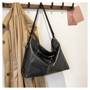 Detail of black leather tote bag with metal buckle hanging on wooden hooks