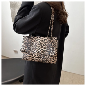 Detail of leopard print shoulder bag with gold chain strap worn over a black blazer