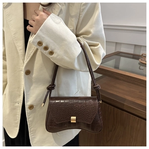 Detail of dark brown crocodile-embossed underarm bag with knot strap and gold clasp