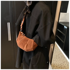 Detail of a brown suede croissant crossbody bag featuring stylish knot-decorated straps