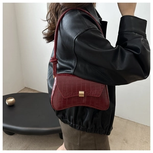 Detail of burgundy crocodile pattern underarm bag with knot strap on leather jacket