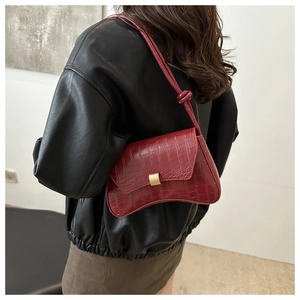 Detail of burgundy crocodile-textured shoulder bag with gold rectangular clasp on a model