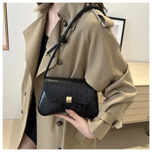 Detail of black crocodile texture shoulder bag with matte gold buckle and knotted strap