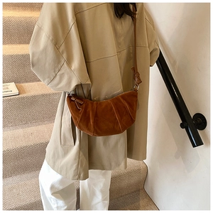 Brown pleated half-moon bag styled with a beige trench coat on a minimalist staircase