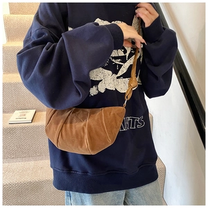 Close-up of brown suede croissant bag with adjustable strap worn by model in a minimalist setting