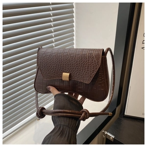 Detail of dark brown crocodile pattern handbag featuring a gold buckle and knotted strap